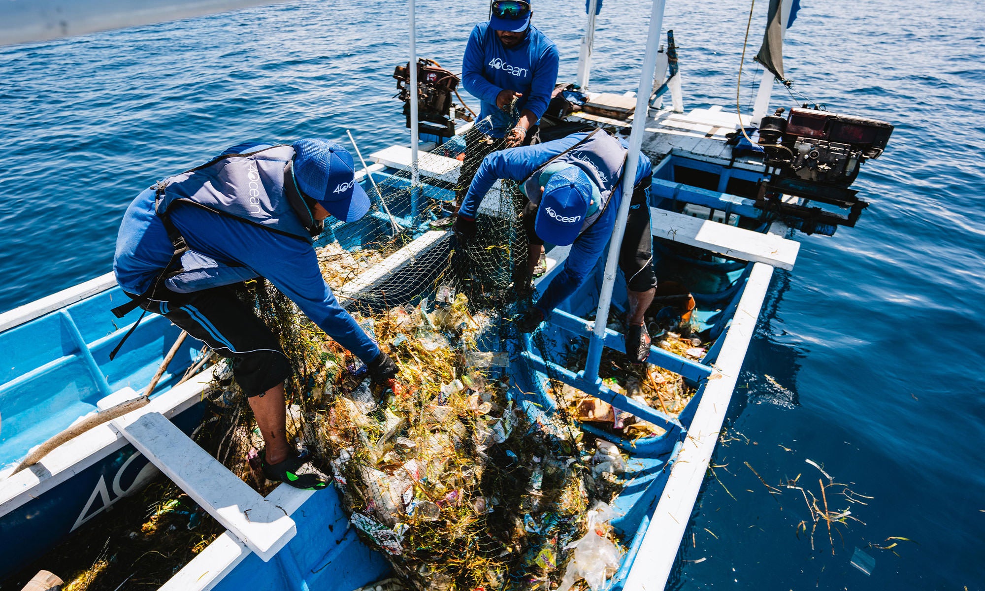 three men on a pontoon boat cleaning up trash from the ocean.