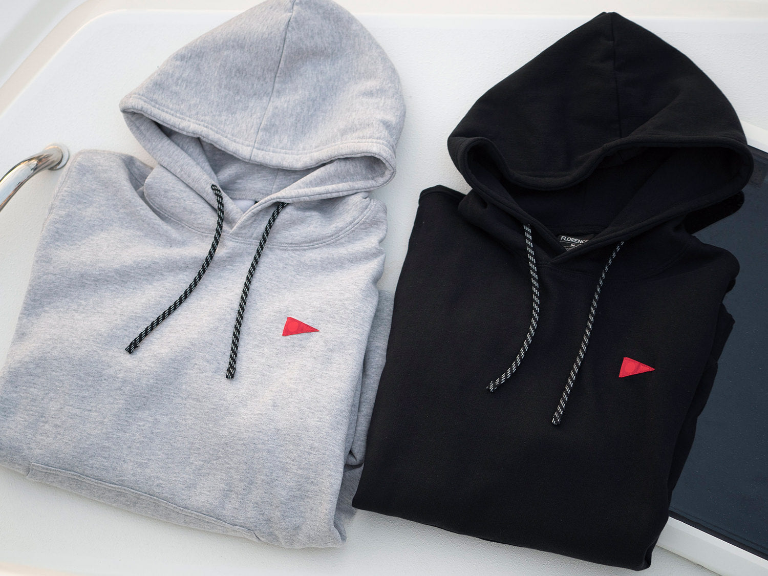 One Light Grey Hoodie and one Black Hoodie, folded up next to eachother