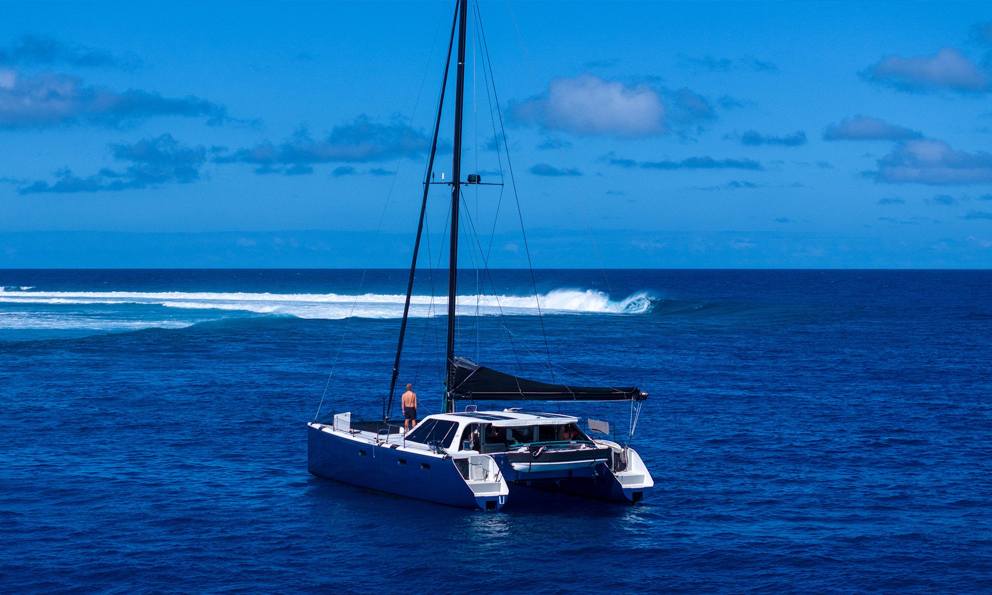 Sailboat on the ocean with a breaking wave in the background and a clear blue sky
