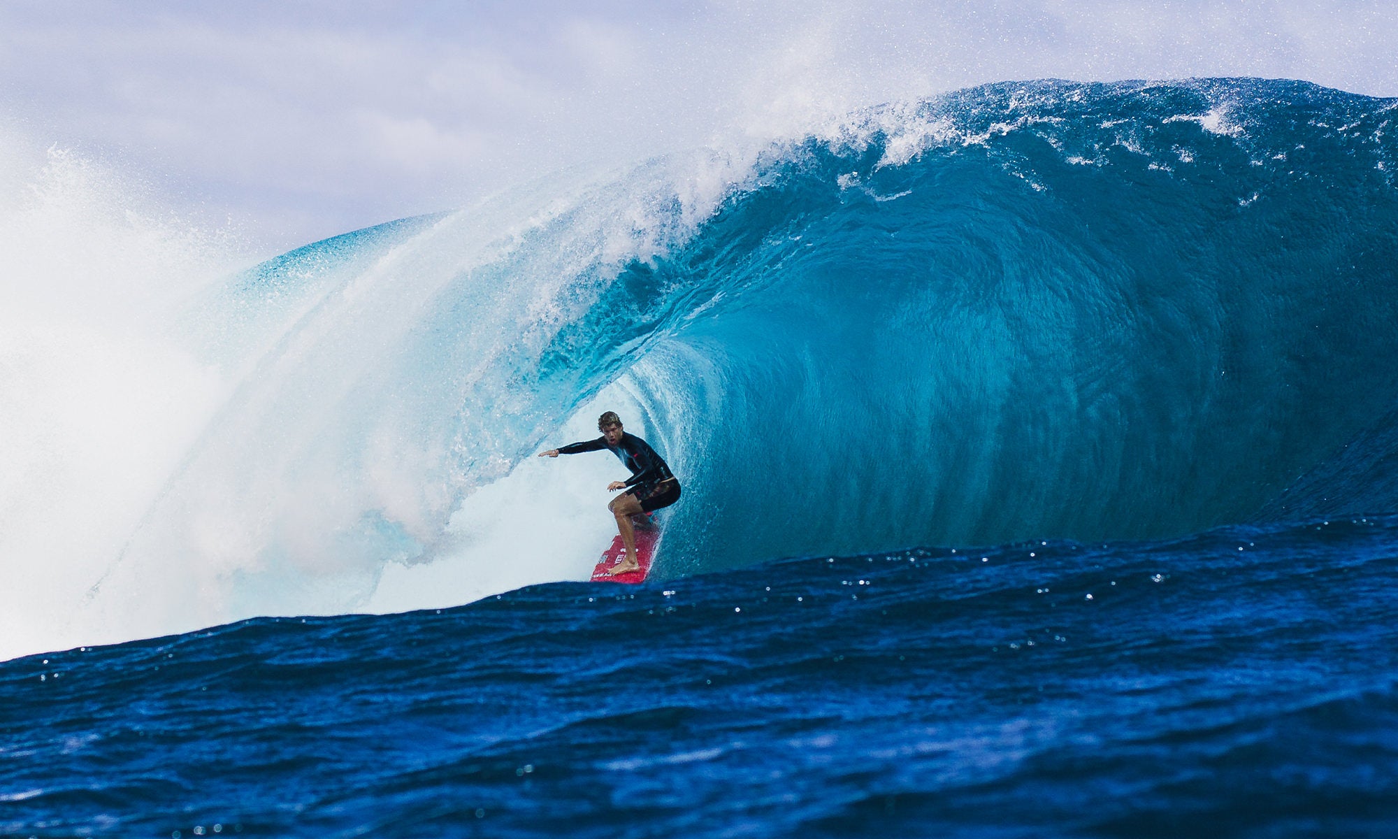 John John Florence getting barreled on a large wave while riding a red surfboard