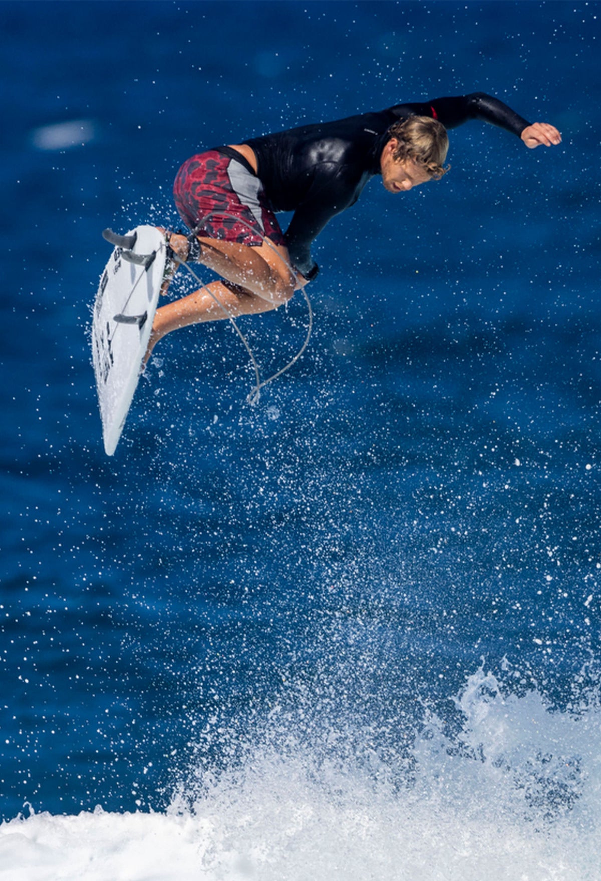 John John Florence in rotation in the air while completing an air trick while surfing, wearing a rashguard and boardshorts