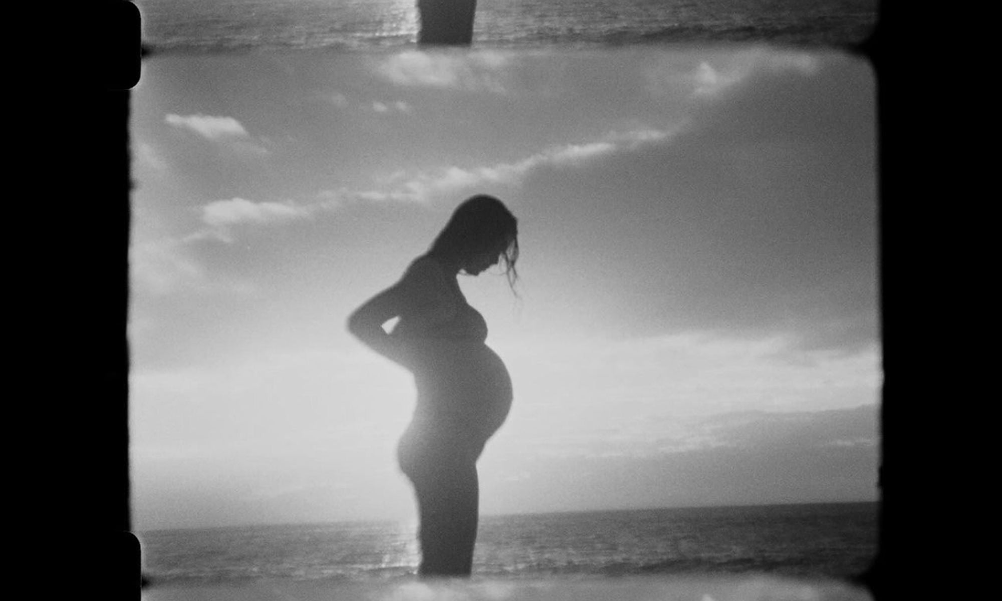 Silohuette photo of a woman who is pregnant with the ocean in the background, in black and white