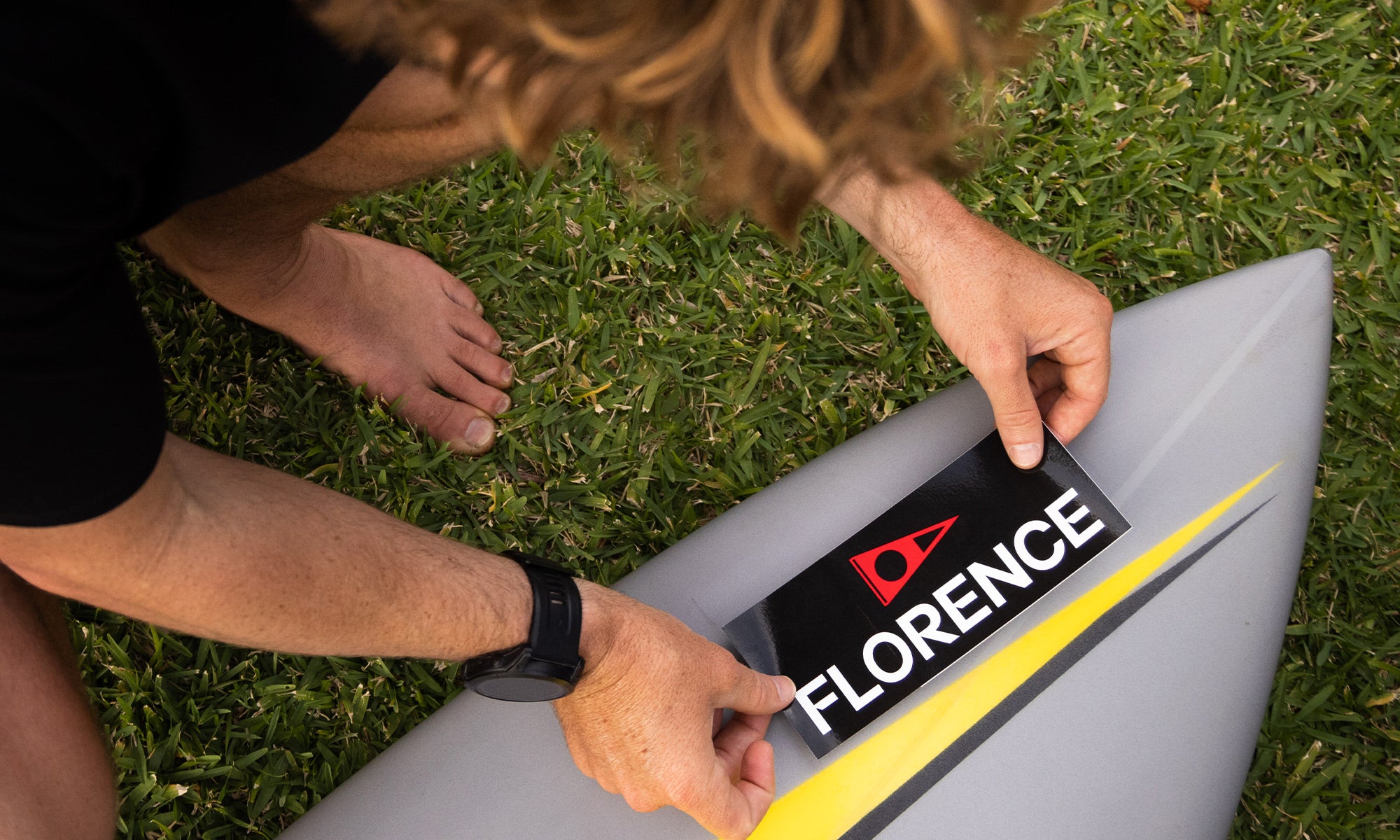 Hands putting a FLORENCE sticker on the nose of a surfboard